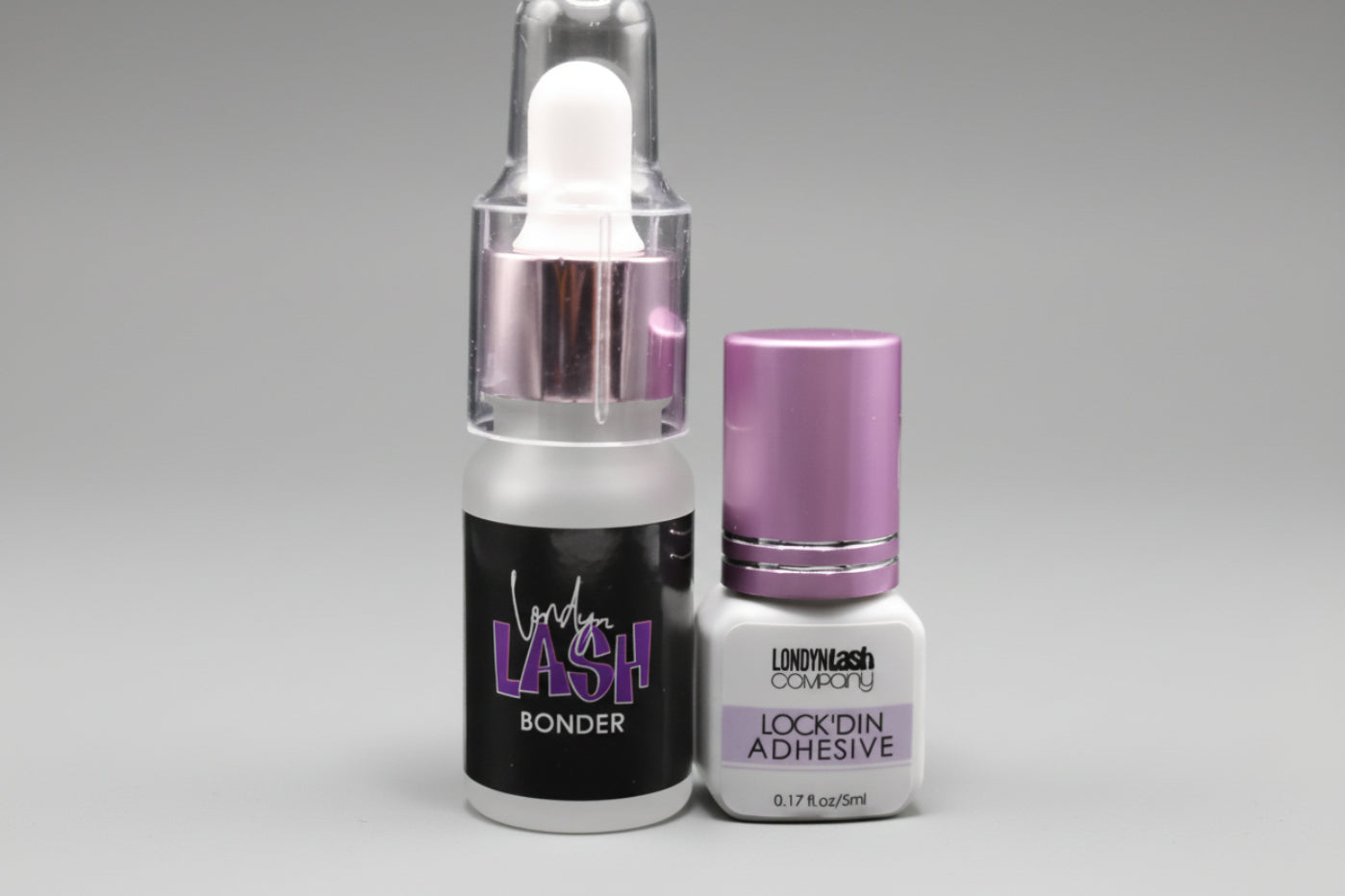Two bottles of eyelash products on a light purple background